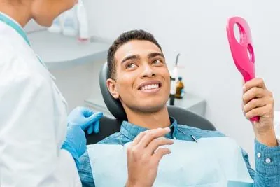 man holding a mirror looking at his smile after a dental checkup at Jay Zimmerman Dentistry