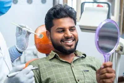 man looking in the mirror at his newly restored smile thanks to restorative services from Jay Zimmerman Dentistry